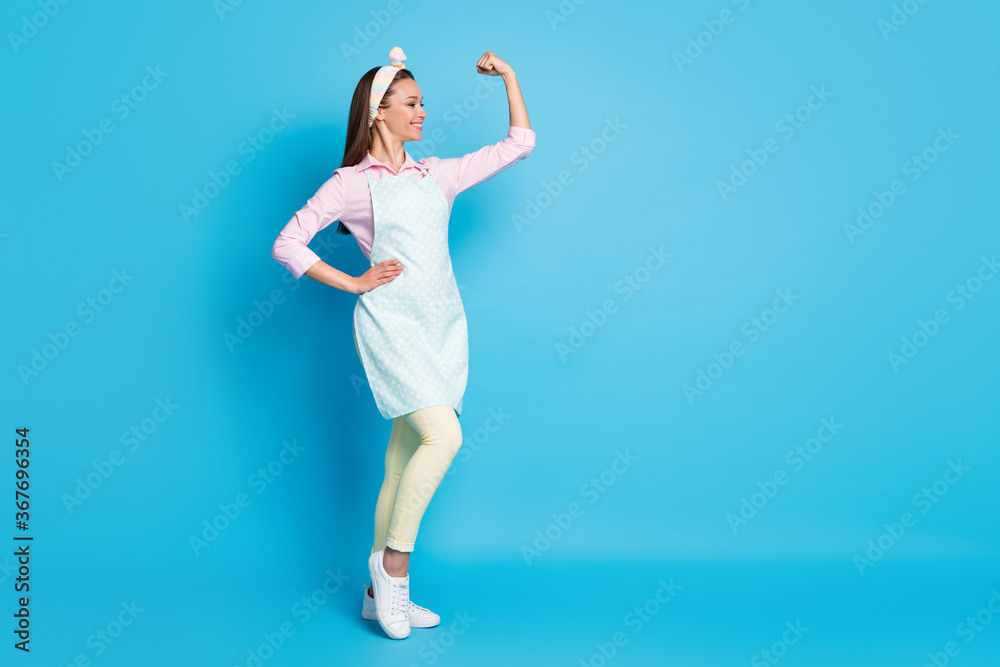 Full length photo of attractive lady confident house wife good mood showing strong muscle arm fist wear headband long dotted apron pink shirt pants shoes isolated blue color background