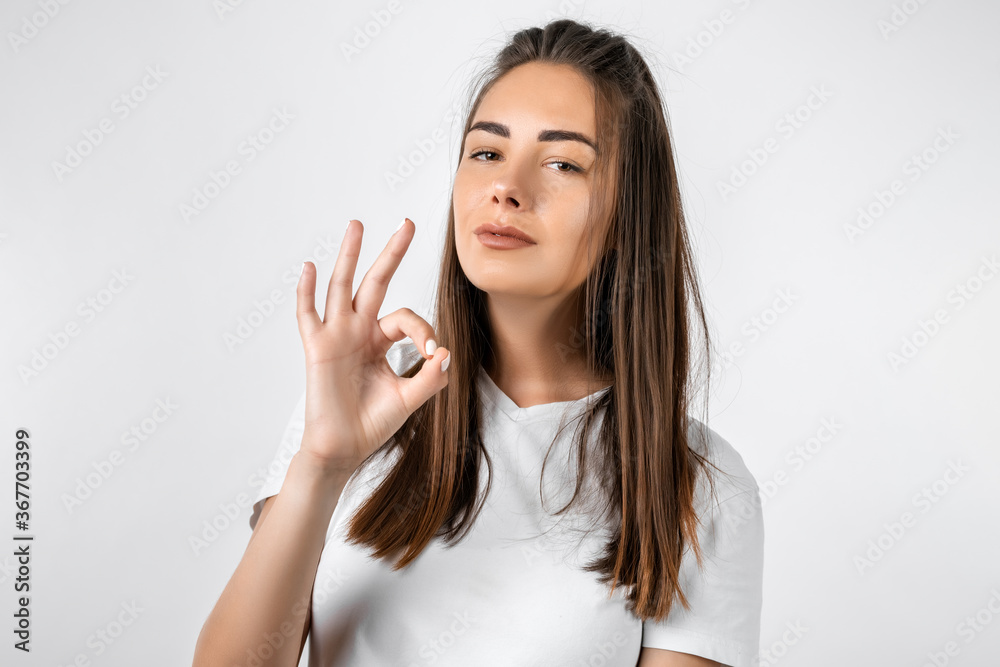 Good job. Pretty carefree modern stylish European girl with long chestnut hair making OK gesture as if saying that everything is finee, white background Good job. Pretty carefree modern stylish European girl with long chestnut hair making OK gesture as if saying that everything is finee, white background