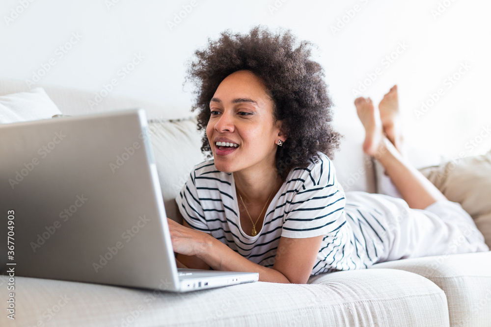 Young beautiful woman with curly hair working on laptop computer while sitting on the sofa at home, heck on oline shops for cyber monday sales. Technology woman concept alternative office freelance Young beautiful woman with curly hair working on laptop computer while sitting on the sofa at home, heck on oline shops for cyber monday sales. Technology woman concept alternative office freelance