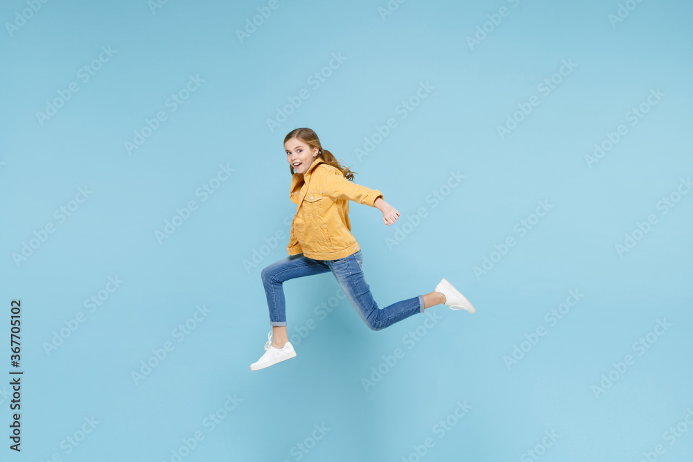 Full length portrait of amazed little blonde kid girl 12-13 years old in yellow jacket isolated on pastel blue background studio. Childhood lifestyle concept. Mock up copy space. Jumping like running. Full length portrait of amazed little blonde kid girl 12-13 years old in yellow jacket isolated on pastel blue background studio. Childhood lifestyle concept. Mock up copy space. Jumping like running.