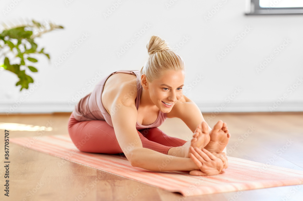 fitness, sport and healthy lifestyle concept - happy smiling young woman doing yoga and seated forward bend at home fitness, sport and healthy lifestyle concept - happy smiling young woman doing yoga and seated forward bend at home