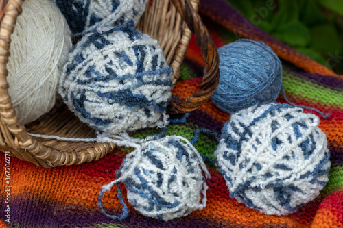 blue and white wool balls in a wicker basket on a multi-colored knitted blanket.