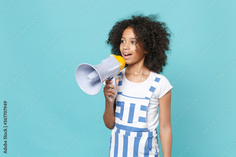 Pretty little african american kid girl 12-13 years old in striped clothes isolated on blue wall background studio portrait. Childhood lifestyle concept. Mock up copy space. Screaming in megaphone. Pretty little african american kid girl 12-13 years old in striped clothes isolated on blue wall background studio portrait. Childhood lifestyle concept. Mock up copy space. Screaming in megaphone.