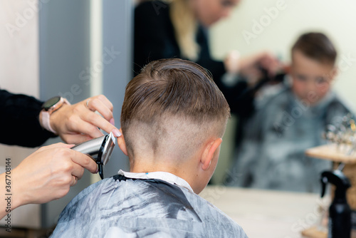 Back view Close up caucasian pretty school boy trendy haircut at bright modern barbershop.
