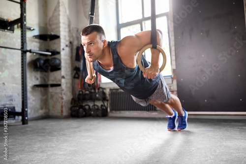 fitness, sport, bodybuilding and people concept - young man doing push-ups on gymnastic rings in gym
