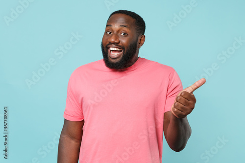Funny young african american man guy in casual pink t-shirt posing isolated on pastel blue background studio portrait. People sincere emotions lifestyle concept. Mock up copy space. Showing thumb up.