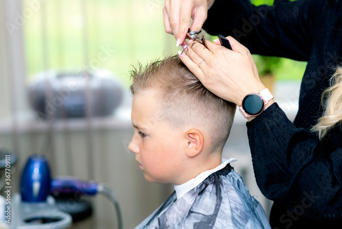 Serious school boy ready getting trendy haircut from expirienced barber at fashionable hairdressing salon.