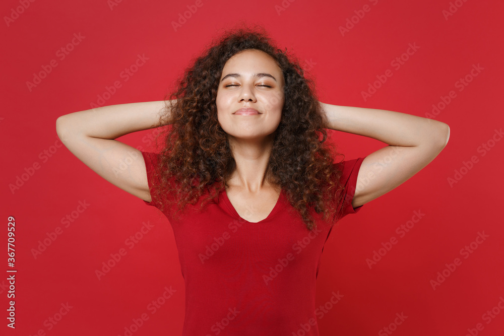 Smiling young african american woman girl in casual t-shirt posing isolated on red wall background studio portrait. People emotions lifestyle concept. Mock up copy space. Sleep with hands behind head. Smiling young african american woman girl in casual t-shirt posing isolated on red wall background studio portrait. People emotions lifestyle concept. Mock up copy space. Sleep with hands behind head.