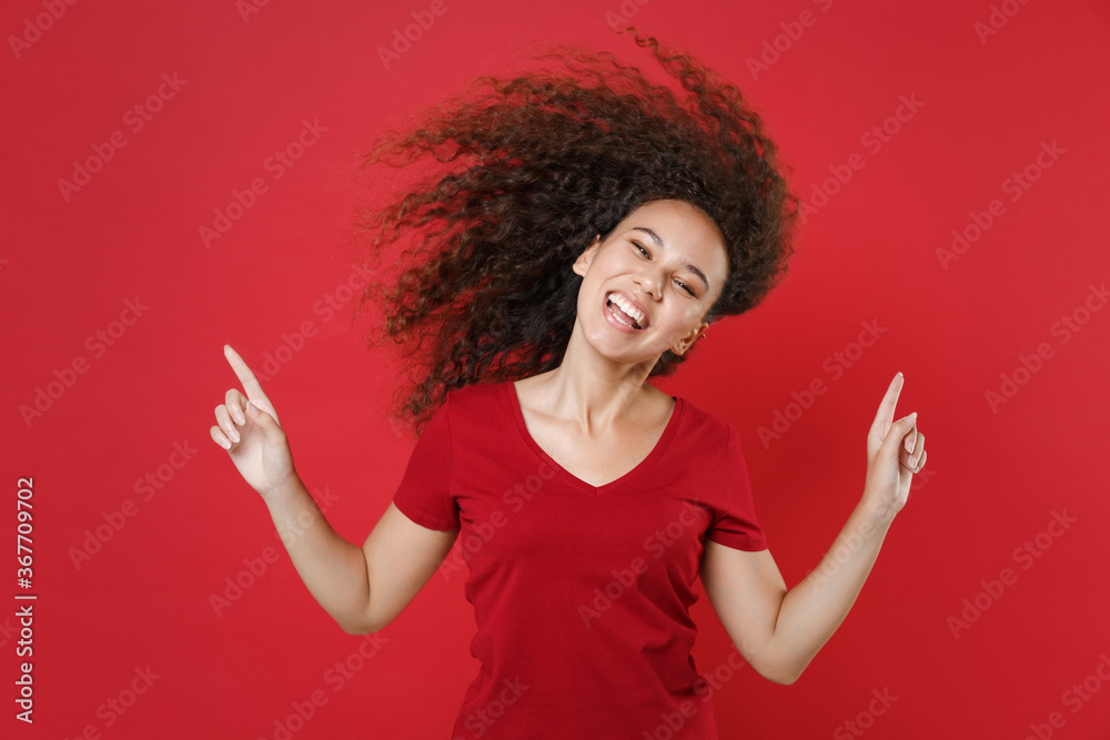 Funny young african american woman girl in casual t-shirt posing isolated on red background. People lifestyle concept. Mock up copy space. Having fun dancing with flying hair point index fingers up. Funny young african american woman girl in casual t-shirt posing isolated on red background. People lifestyle concept. Mock up copy space. Having fun dancing with flying hair point index fingers up.
