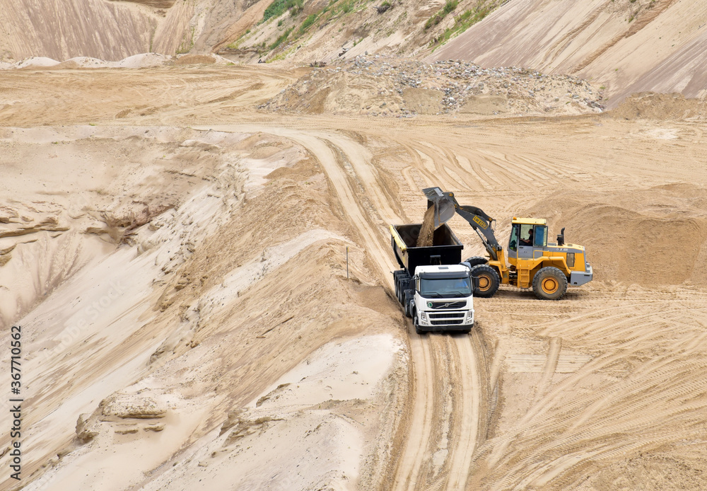 Wheel front-end loader loading sand into heavy dump truck at the opencast mining quarry. Dump truck transports sand in open pit mine. Quarry in which sand and gravel is excavated from the ground. Wheel front-end loader loading sand into heavy dump truck at the opencast mining quarry. Dump truck transports sand in open pit mine. Quarry in which sand and gravel is excavated from the ground.