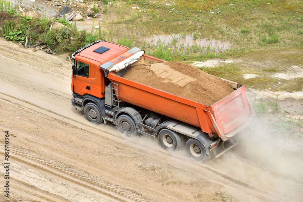 Fototapeta premium Dump truck transports sand in open pit mine. In the production of concrete, concrete for the construction using coarse sand. Quarry in which sand and gravel is excavated from ground. Mining industry