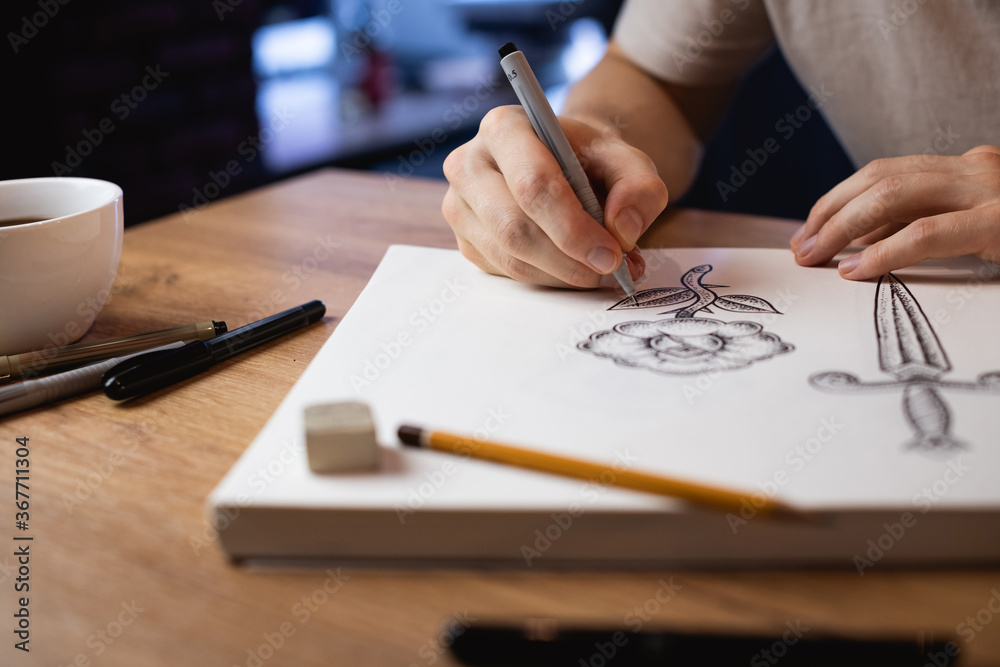 Cropped view of artist drawing sketches beside coffee cup and markers on table Cropped view of artist drawing sketches beside coffee cup and markers on table
