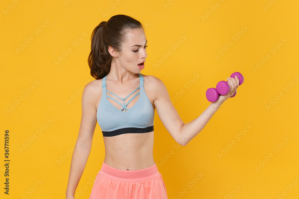 Shocked young fitness sporty woman girl in sportswear working out isolated on yellow background studio. Workout sport motivation lifestyle concept. Mock up copy space. Doing exercise with dumbbells. Shocked young fitness sporty woman girl in sportswear working out isolated on yellow background studio. Workout sport motivation lifestyle concept. Mock up copy space. Doing exercise with dumbbells.