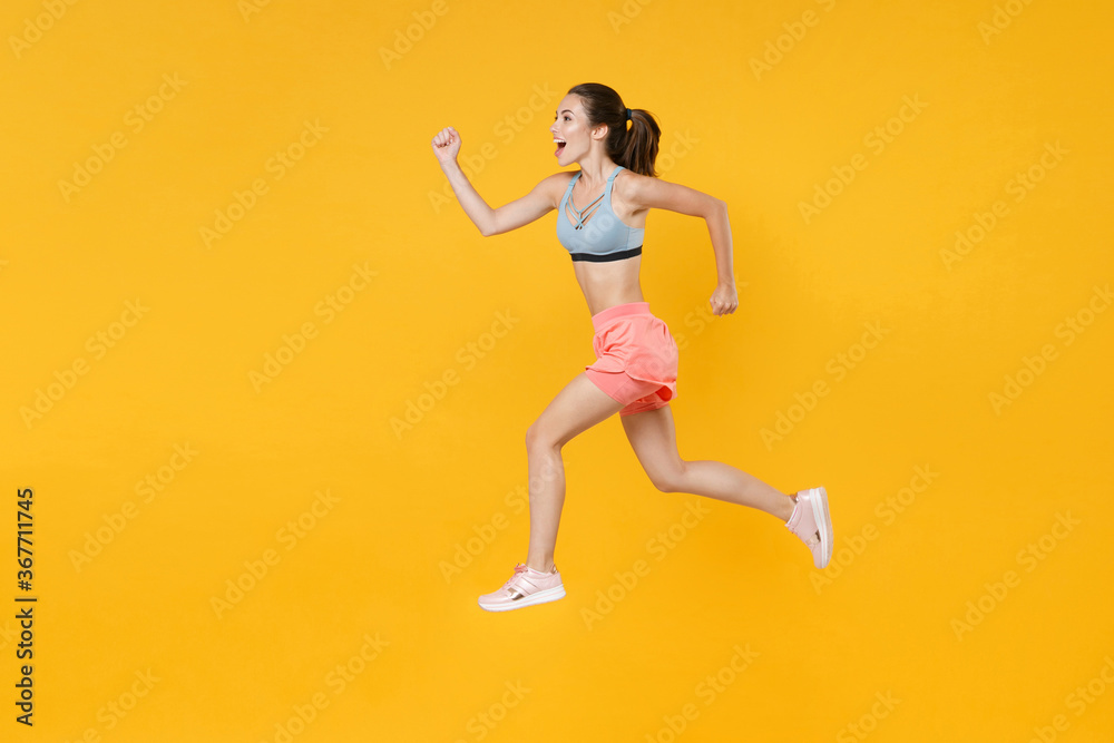 Full length portrait of excited fitness woman girl in sportswear working out isolated on yellow background studio. Workout sport motivation lifestyle concept. Mock up copy space. Jumping like running.