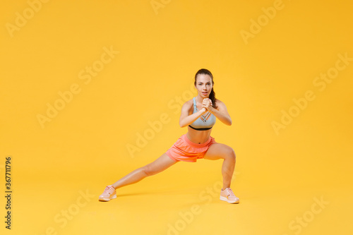 Full length portrait of beautiful young fitness woman in sportswear working out isolated on yellow background. Workout sport motivation lifestyle concept. Mock up copy space. Doing exercise lunge.