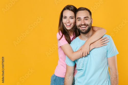 Cheerful young couple two friends guy girl in blue pink t-shirts posing isolated on yellow wall background studio portrait. People sincere emotions lifestyle concept. Mock up copy space. Hugging.
