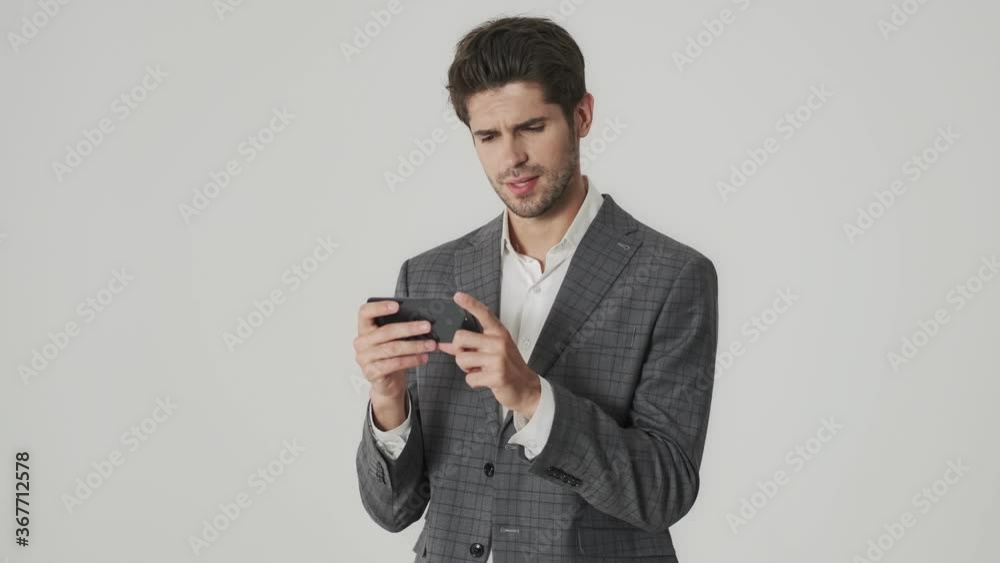 Young concentrated business man isolated over white wall background while using mobile phone Young concentrated business man isolated over white wall background while using mobile phone