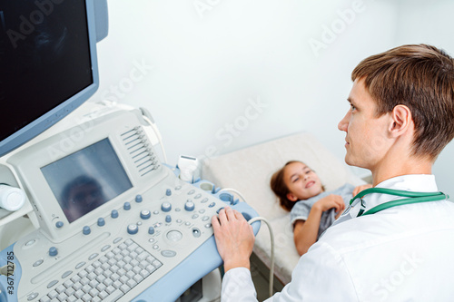 Foused on his task doctor performing ultrasound scan on a ten year old girl photo
