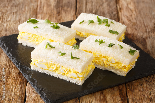 Egg salad tucked between slices of white bread, Japanese egg sandwich Tamago Sando close-up on a slate board on the table. Horizontal