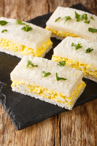 Egg salad tucked between slices of white bread, Japanese egg sandwich Tamago Sando closeup on the board. Vertical