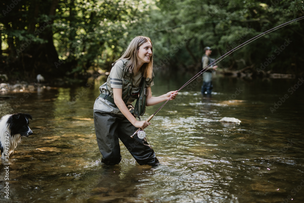 Young adult couple with dog is fishing together on fast mountain river. Active people and sport fly fishing concept. Young adult couple with dog is fishing together on fast mountain river. Active people and sport fly fishing concept.