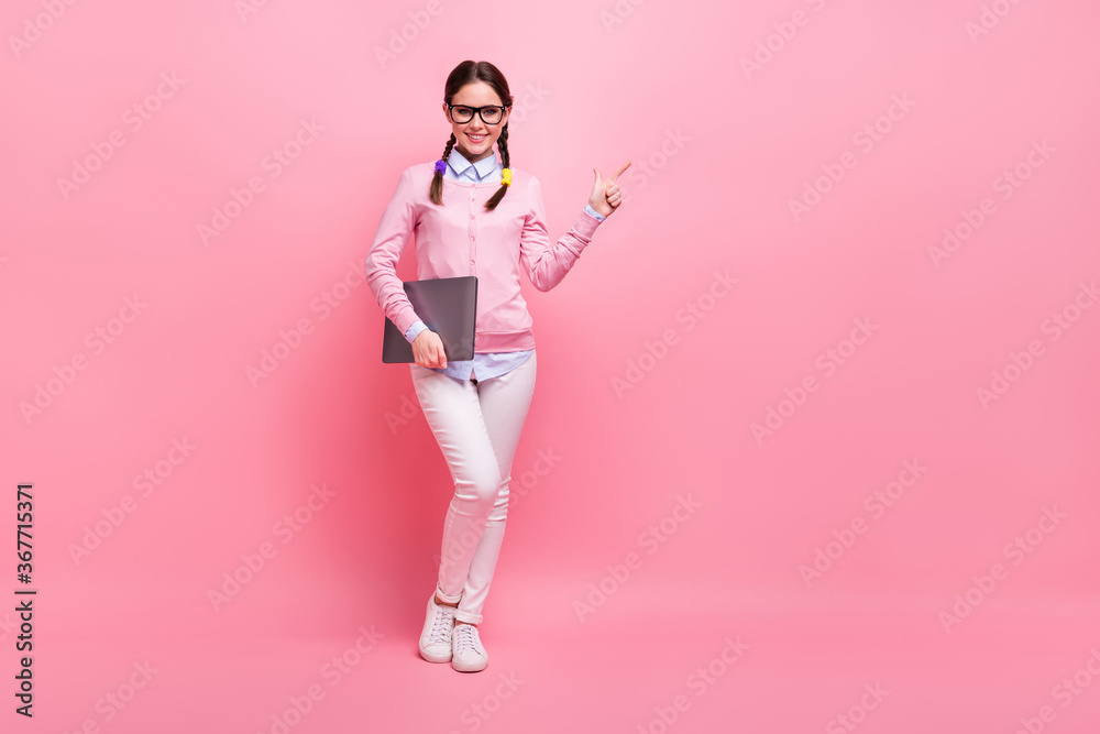 Full length body size view of her she nice cheerful confident brown-haired teenage girl holding in hand laptop demonstrating copy space advert learn study isolated pink pastel color background Full length body size view of her she nice cheerful confident brown-haired teenage girl holding in hand laptop demonstrating copy space advert learn study isolated pink pastel color background
