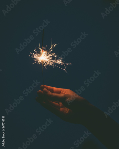 Person holding a sparkler and spark flying away in hand during night