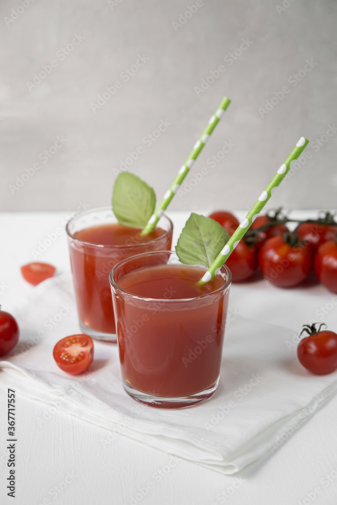 Two glasses with tomato juice stand on a light background, decorated with tubes and mint leaves, next to it are tomato slices Two glasses with tomato juice stand on a light background, decorated with tubes and mint leaves, next to it are tomato slices