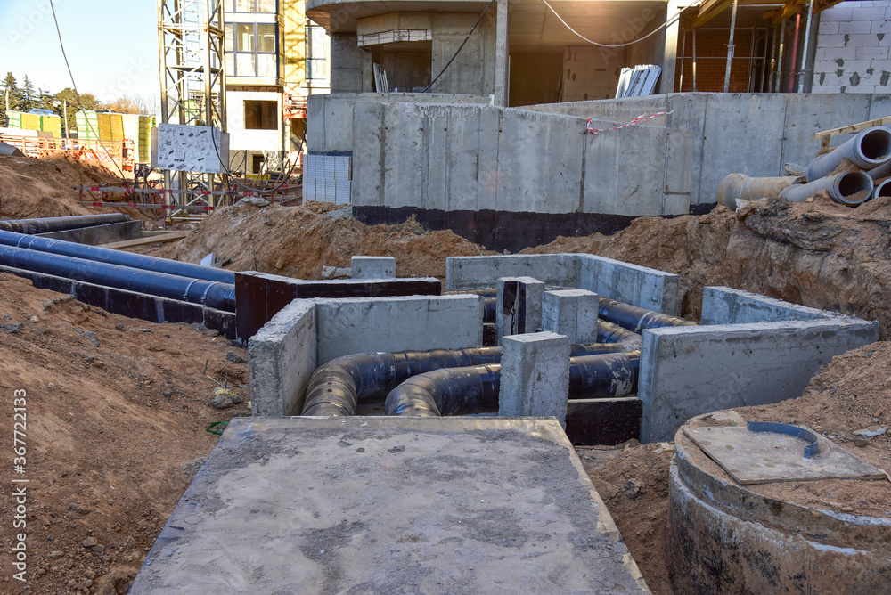 Laying heating pipes in a trench at construction site. Install underground storm systems of water main and sanitary sewer. Cold and hot water, heating and heating system of apartments in the house Laying heating pipes in a trench at construction site. Install underground storm systems of water main and sanitary sewer. Cold and hot water, heating and heating system of apartments in the house