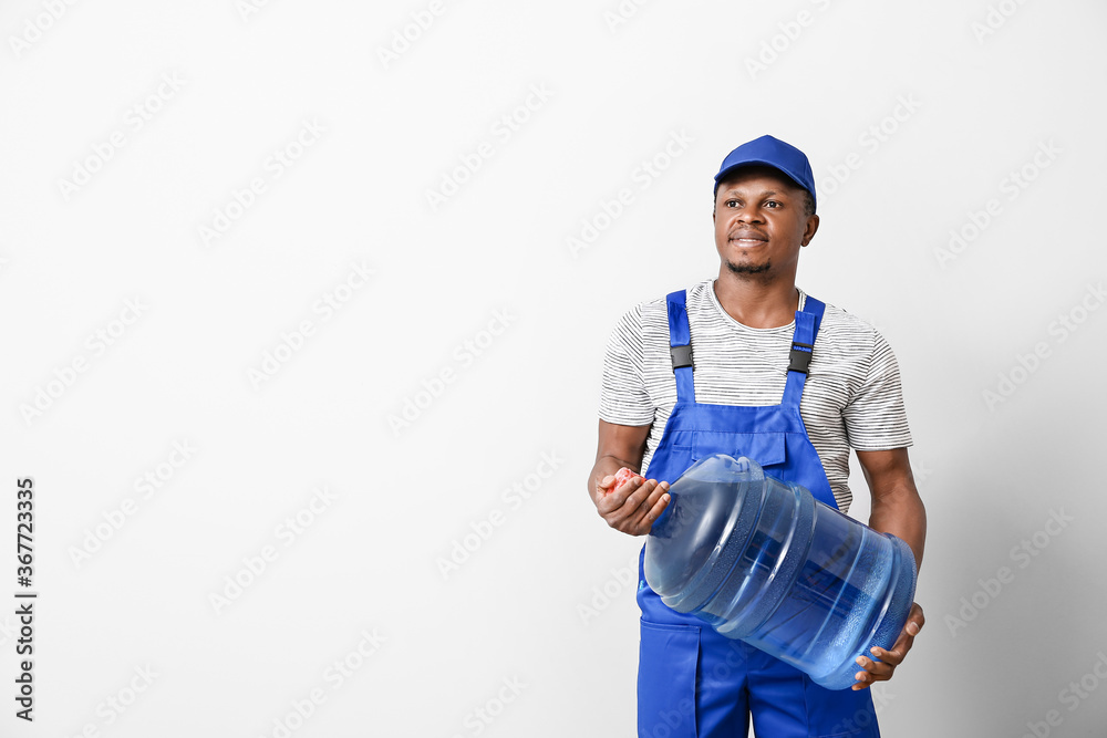 African-American delivery man with bottle of water on light background African-American delivery man with bottle of water on light background