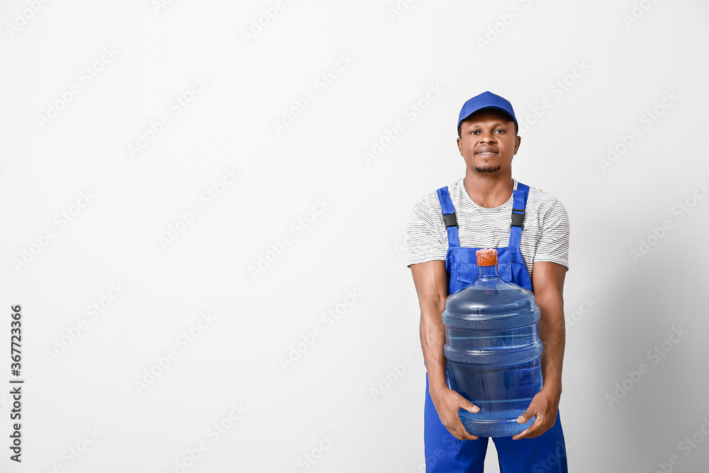 African-American delivery man with bottle of water on light background African-American delivery man with bottle of water on light background