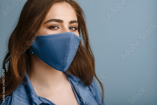 Beautiful Woman wearing stylish protective blue face mask. Trendy Fashion accessory during quarantine of coronavirus pandemic. Close up studio portrait. Copy, empty space for text