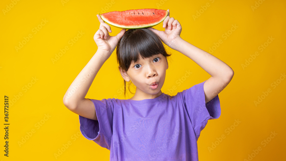 Portrait of young Asian girl holding watermelon on head with cheeky face, Thai attractive student kid looking camera with happiness isolated in studio on orange background Portrait of young Asian girl holding watermelon on head with cheeky face, Thai attractive student kid looking camera with happiness isolated in studio on orange background