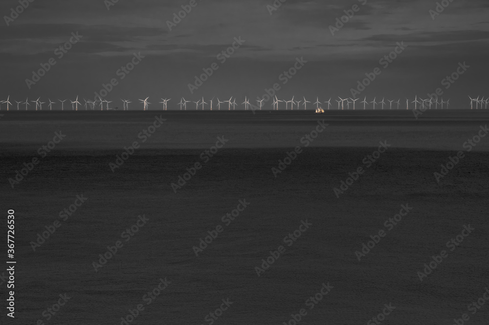Dark impression of a row of windmills at the horizon in the sea with a sailing yacht
