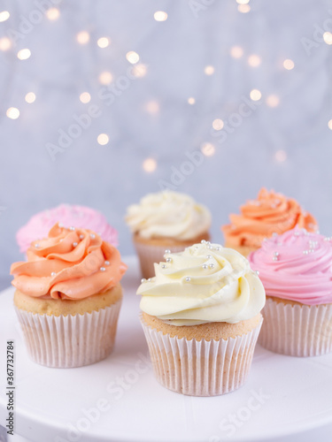 Cupcakes with pink, orange and white cream, selective focus on blurred lights background with copy space, closeup. Celebration concept.