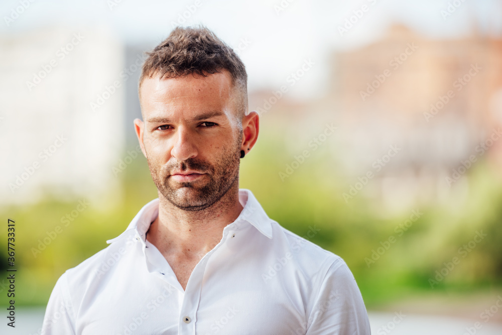 young man in white shirt looking at camera with short hair and short beard outdoors young man in white shirt looking at camera with short hair and short beard outdoors
