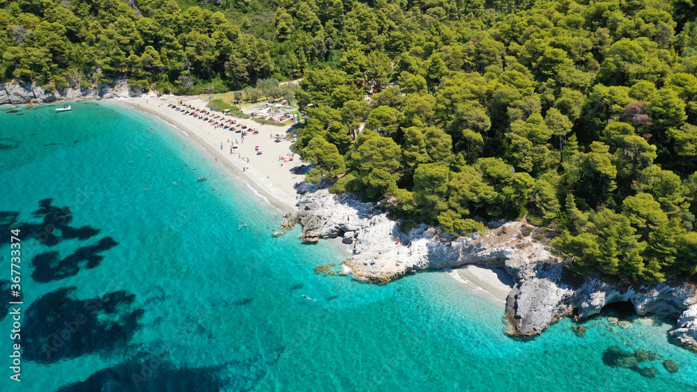 Aerial drone photo of secluded rocky cove near turquoise pebble paradise beach of Kastani covered with pine trees, Skopelos island, Sporades, Greece