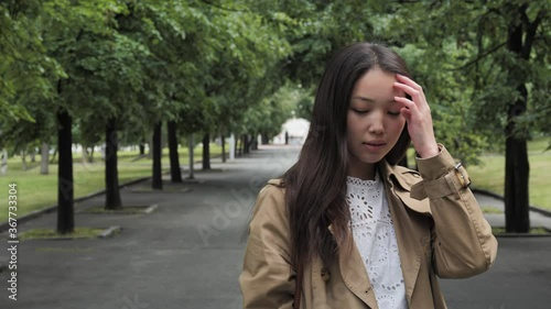 A young pretty girl in a brown trench and white blouse poses for the camera in a city park. High quality 4k footage