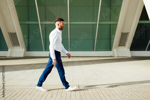 young man in white shirt  blue pants and short beard walking sideways to camera