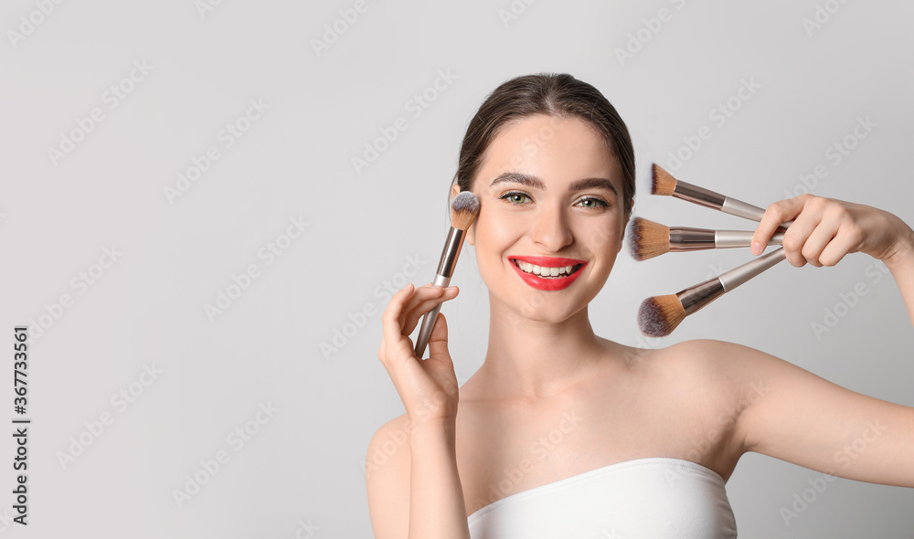 Young woman with makeup brushes on light background Young woman with makeup brushes on light background