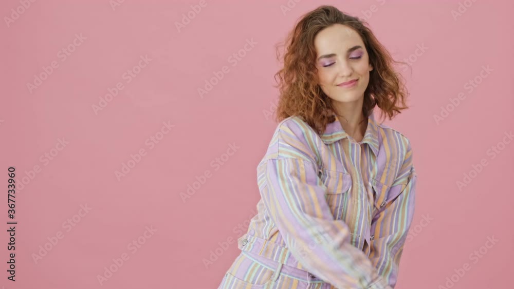 A happy young woman is dancing isolated over pink background in studio