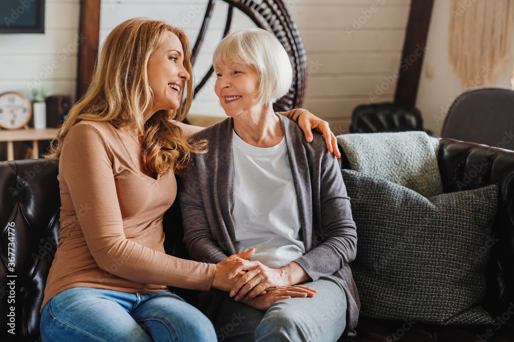© InsideCreativeHouse - Senior mother with adult daughter hugging each other on sofa in living room
