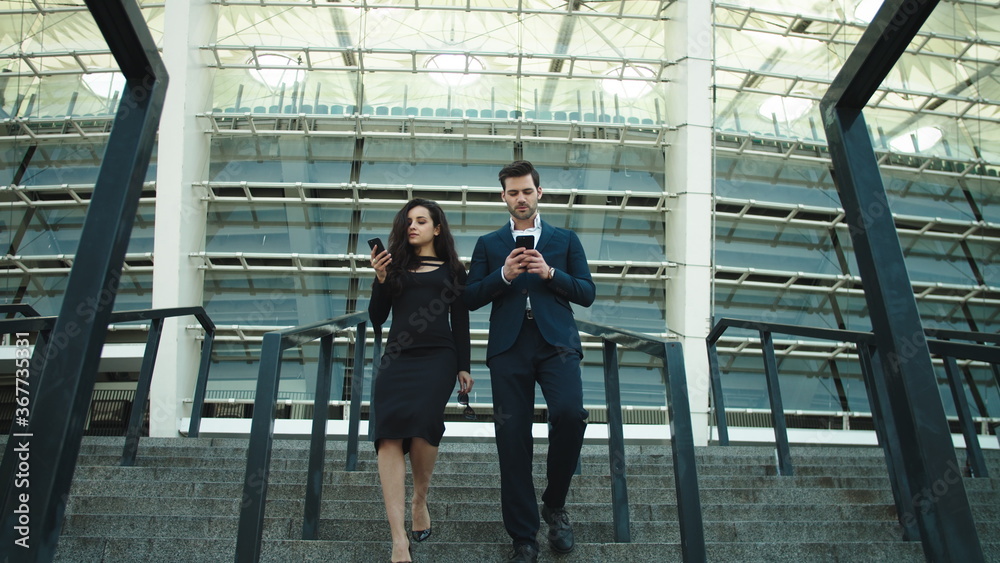 Couple walking with mobile phones. Couple using smartphones together at street Couple walking with mobile phones. Couple using smartphones together at street