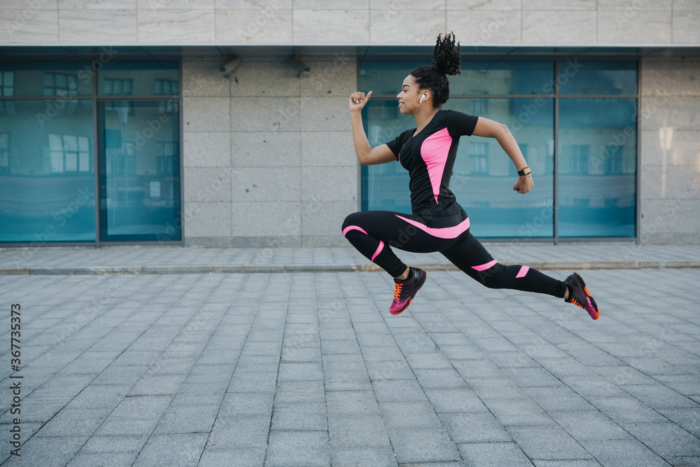 Exercise for weight loss. Woman in sportswear with wireless headphones frozen in air, jumping while running
