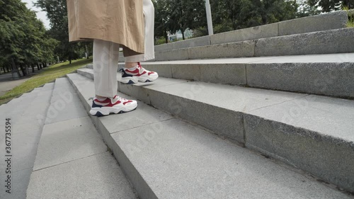 A girl in trousers and trench climbs the steps on the street. Women's feet in close-up sneakers. High quality 4k footage