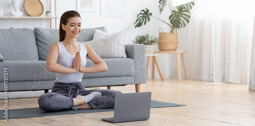 Peaceful young woman meditating at home  using laptop