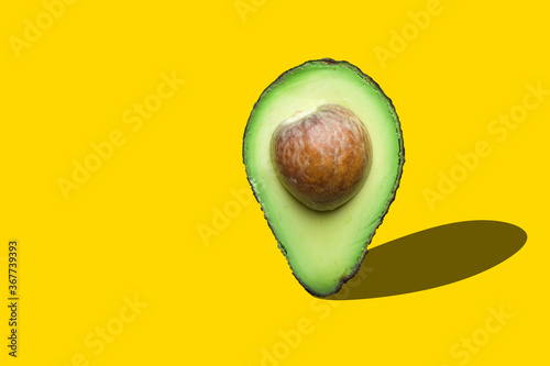 Raw ripe halved avocado with pit imitating map pointer with drop shadow on yellow background. Creative food poster banner for vegan healthy oil diet concept photo