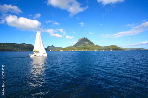 White siling boat with bora bora island in background, turquoise water, overwater bungalows in French polynesia, Bora Bora, Tahiti.