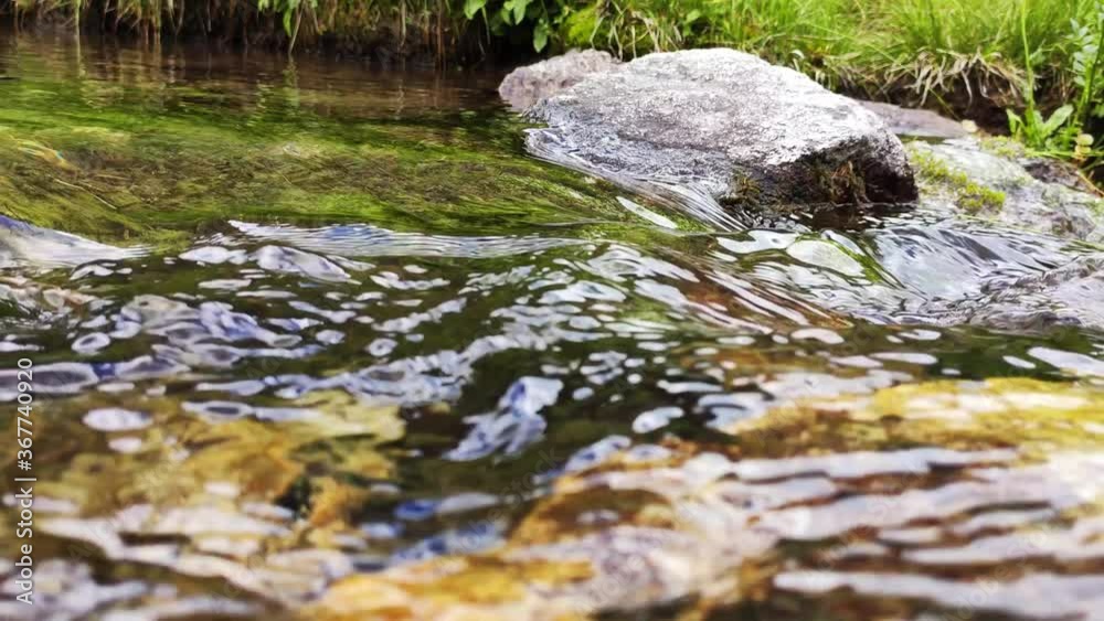 Close-up view mountain stream with stone and sky reflections. Flowing river with smooth stones. Spring water running through stones and green grass Close-up view mountain stream with stone and sky reflections. Flowing river with smooth stones. Spring water running through stones and green grass