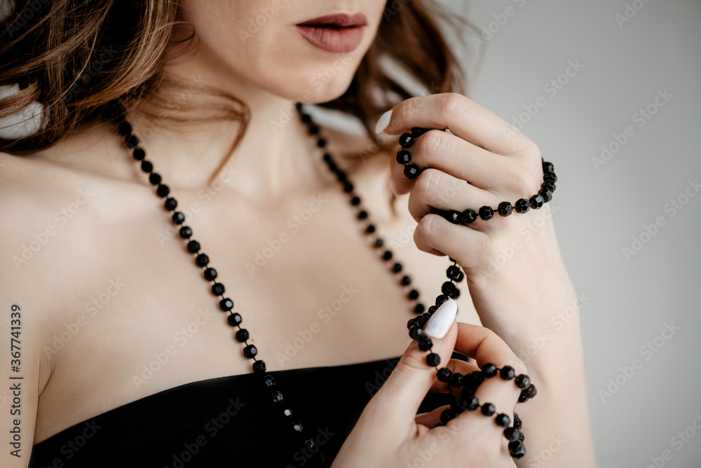 Attractive caucasian girl in a black dress twirled a string of beads around her fingers